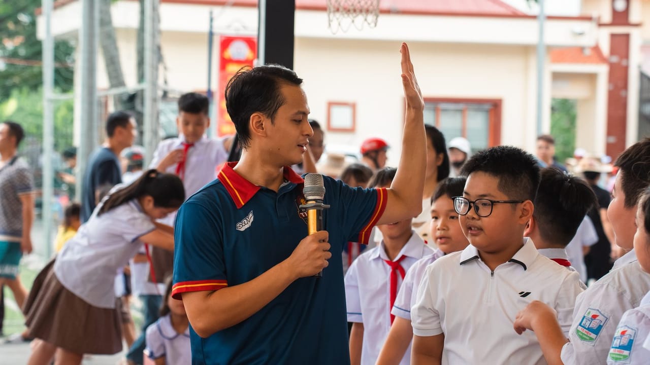 Huấn luyện viên Hanoi Titans cầm micro đập tay cùng một học sinh tiểu học trong sân trường