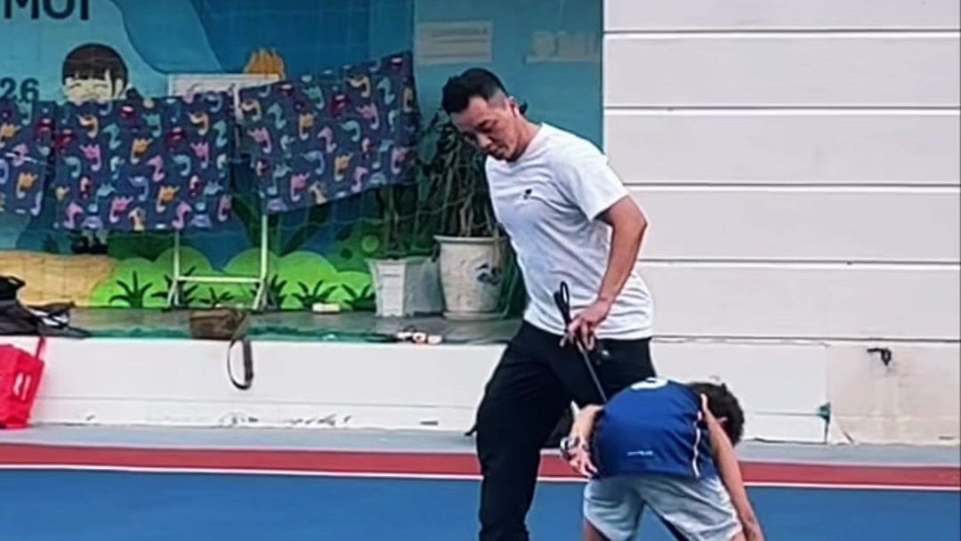 Huấn luyện viên đứng cạnh một học viên đang cúi người chạm cọc trong bài kiểm tra khéo léo trên sân