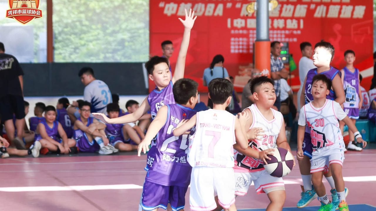Các cầu thủ nhí áo tím và áo trắng tranh bóng dưới rổ trong nhà thi đấu ở Bằng Tường