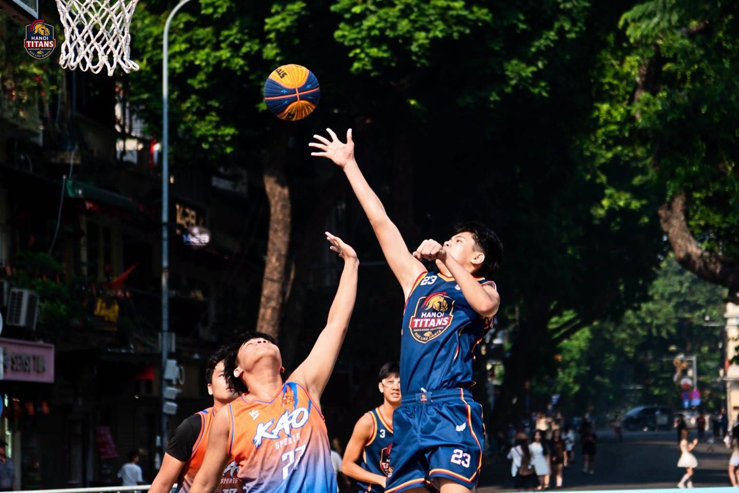 Hai cầu thủ bật cao tranh bóng ở giữa sân, cầu thủ áo xanh navy in chữ Hanoi Titans vươn tay chạm bóng trước