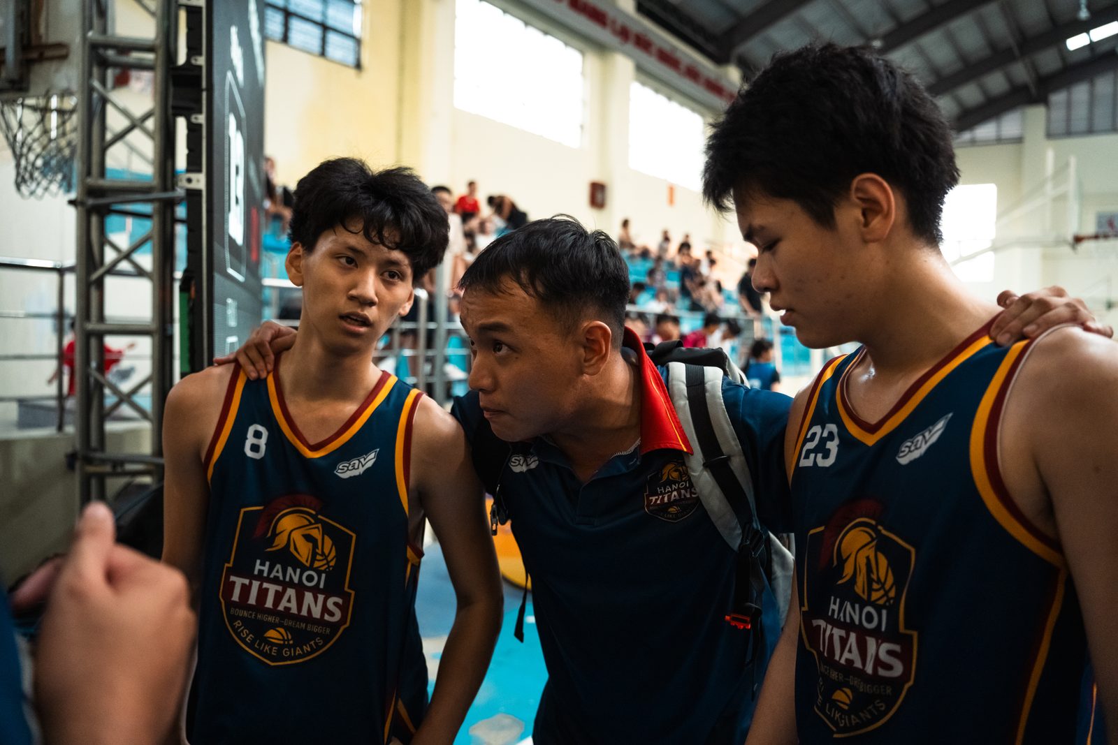 Ba cầu thủ U15 Hanoi Titans đứng cạnh huấn luyện viên trao đổi trên sân